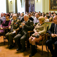 Grupa kilkudziesięciu osób zgromadzona na sali ratuszowej, w tle duży obraz na ścianie.