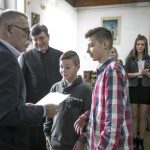 Starszy mężczyzna wręcza chłopcom dyplom, z tyłu widać innych ludzi.