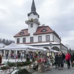 Stoiska ze świątecznymi artykułami, z nimi oglądający je ludzie i budynek ratusza.