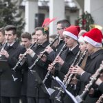 Dziewczynki i chłopcy grający na instrumentach muzycznych w orkiestrze, niektórzy mają na głowie czapki mikołajowe.