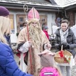 Mężczyzna przebrany za świętego Mikołaja oraz otaczający go ludzie i dzieci, w tle budynek,