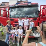 Kobieta robi zdjęcie telefonem grupce dzieci stojących na tle wozu strażackiego.