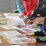 Chłopiec przygląda się rozłożonym na stole fotografiom, obok niego inne dzieci.