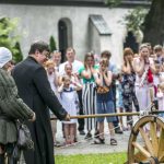 Ksiądz zapalający dawną armatę, obok mężczyzna w średniowiecznym stroju, z tyłu zgromadzeni ludzie.