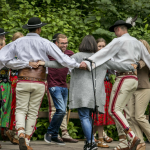 Tańcząca na scenie w kółku grupa osób na scenie, osoby w góralskich strojach.