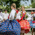 Tańczące na scenie kobiety w góralskich strojach i mężczyźni tańczący na scenie.