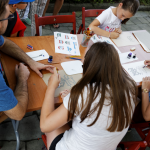 Mężczyzna i trzy dziewczynki siedzą przy stoliku, dziewczynki rysują na kartkach papieru.