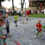 Kilkoro dzieci bawi się przykościelnym placu, z tyłu białe namioty i mury miasta.