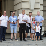 Pięciu mężczyzn i dwóch chłopców stojących pod budynkiem ratusza, przed nimi dwóch chłopców.