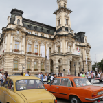 Dwa zabytkowe samochody stojące na rynku przed budynkiem ratusza, w tle tłum ludzi.