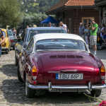 Tył czerwonego, zabytkowego samochodu typu Volkswagen, przed nimi inne auta, obok zwiedzający ludzie.