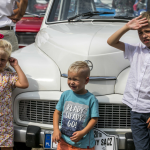 Trójka dzieci stojąca przed białym samochodem.