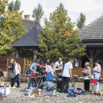 Kilkanaście osób zgromadzonych na rynku miasteczka, oglądających pamiątki na rozłożonym stoisku.