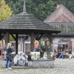 Drewniane zabudowania na rynku miasteczka i wiszące na nich obrazy, oglądający je ludzie.