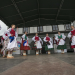 Grupa dziewcząt tańcząca na scenie w strojach ludowych.