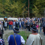 Duża grupa ludzi zgromadzona na polanie, z tyłu las.