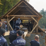 Grupa ludzi wchodząca do drewnianego budynku.