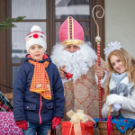 Mały chłopiec, obok św. Mikołaj i dziewczyna przebrana za śnieżynkę, obok prezenty.