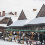 Stoiska z ozdobami, przy stoiskach ludzie, z tyłu drewniane budynki.