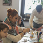 Kobieta i mężczyzna wykonują ozdoby, obok siedzi mała dziewczynka.