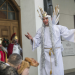 Mężczyzna przebrany za anioła, za nim budynek, obok ludzie w przebraniach.