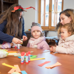 Dziewczynki robią ozdoby świąteczne z papieru, przy stole, z tyłu okno.