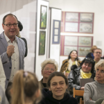 Zgromadzona na sali publiczność, po lewej stronie stoi mężczyzna i kobiety.