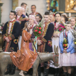 Figurka Chrystusa na osiołku, z tyłu ludzie w regionalnych strojach zgromadzeni we wnętrzu kościoła.