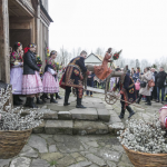 Mężczyźni w strojach ludowych wynoszący z kościoła figurę Chrystusa na osiołku, obok ludzie w strojach ludowych, ksiądz.