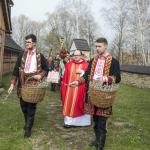 Mężczyźni w strojach regionalnych z koszami bazi, z tyłu ksiądz i wierni.