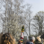 Odwróceni tyłem ludzie, kobieta z palmą wielkanocną, drzewa.