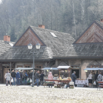 Stoiska ze świątecznymi wyrobami, z tyłu drewniane domy i drzewa.