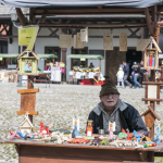 Mężczyzna za stoiskiem z drewnianymi figurkami, z tyłu stoiska.