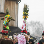 Ludzie w strojach regionalnych zebrani przed kościołem trzymający palmy.