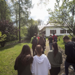 Grupka młodzieży idąca drogą, przed nimi biały dwór, po bokach drzewa.