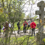 Grupa młodzieży na drodze, na pierwszym planie zarośla i kamienny krzyż.