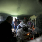 Grupa ludzi zgromadzona w kuchni starego domu, palenisko.