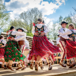 Góralskie pary tańczące na scenie, z tyłu drzewa i chmury.