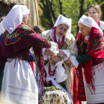 Kobiety w góralskich strojach ubierają dziewczynce czepiec na głowę, obok inne kobiety.