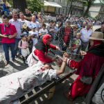 Leżący na machinie do tortur mężczyzna, wokoło niego zebrani ludzie, mężczyzna z kamerą.