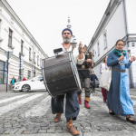 Mężczyzna trzymający kocioł - instrument, obok dziewczyna w długiej sukni z tamburynem.