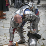 Mężczyzna przebrany za rycerza, podnosi z ziemi tarczę, w drugiej ręce trzyma hełm.