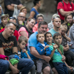 Siedzący na ławkach dorośli i dzieci.