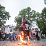 Przeskakująca przez ogień kobieta w dawnym stroju, z tyłu publiczność.