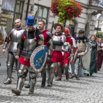 Grupa osób w historycznych strojach idąca deptakiem.