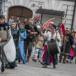 Grupa osób w historycznych strojach idąca ulicą.