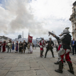 Grupa osób w historycznych strojach zgromadzona na rynku.