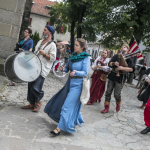 Grupa osób w historycznych strojach idąca ulicą, na pierwszym planie muzycy grający na dawnych instrumentach.