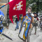 Mężczyźni w rycerskich zbrojach, jeden trzymający sztandar, drugi tarczę z wizerunkiem świętej Kingi.