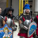 Grupa osób w strojach historycznych zebrana na kościelnym dziecińcu.